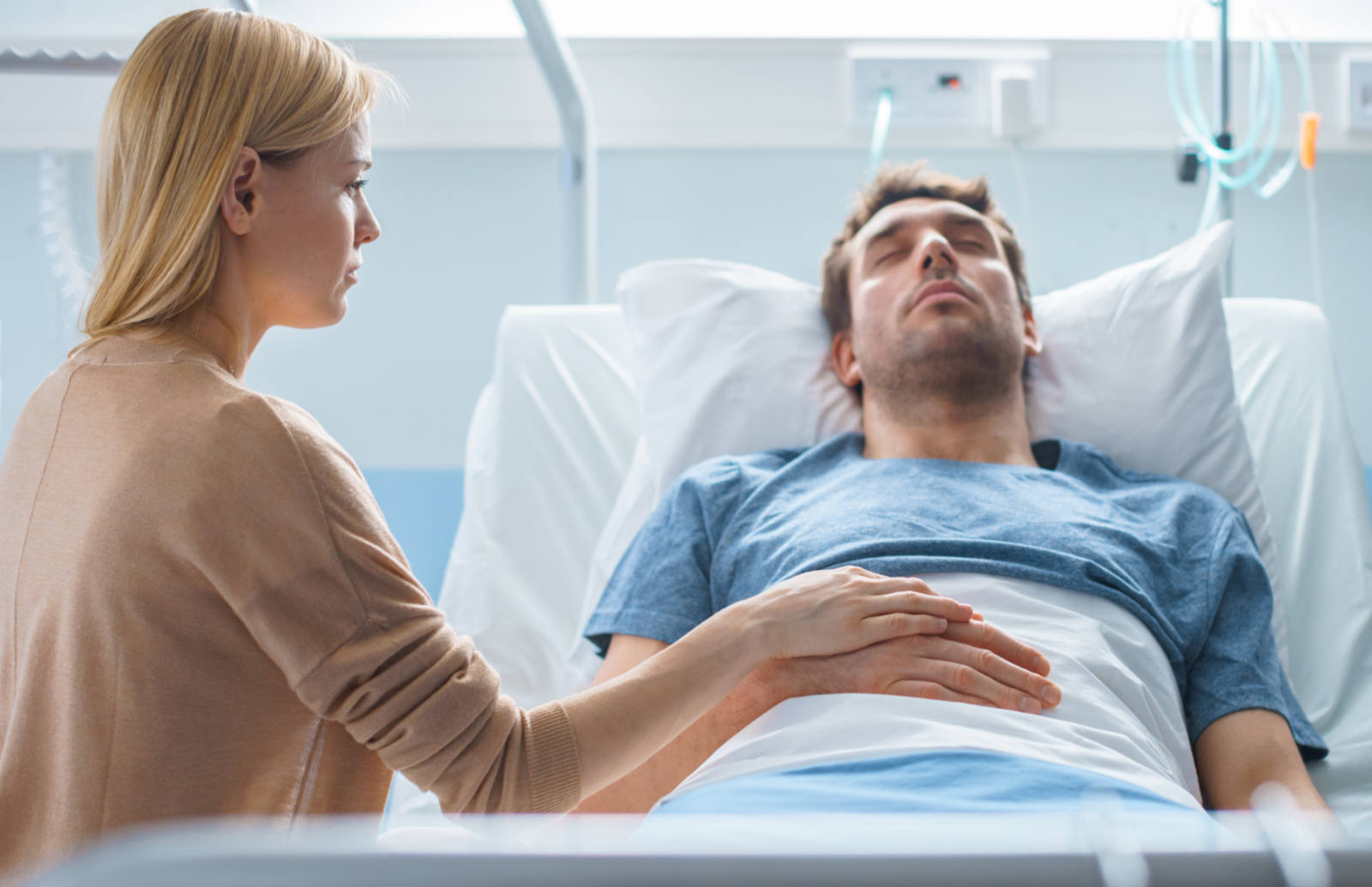 man laying in a hospital bed with a women sitting next to him