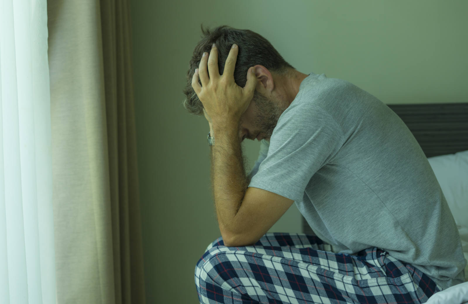 man sitting on the edge of a bed holding his head