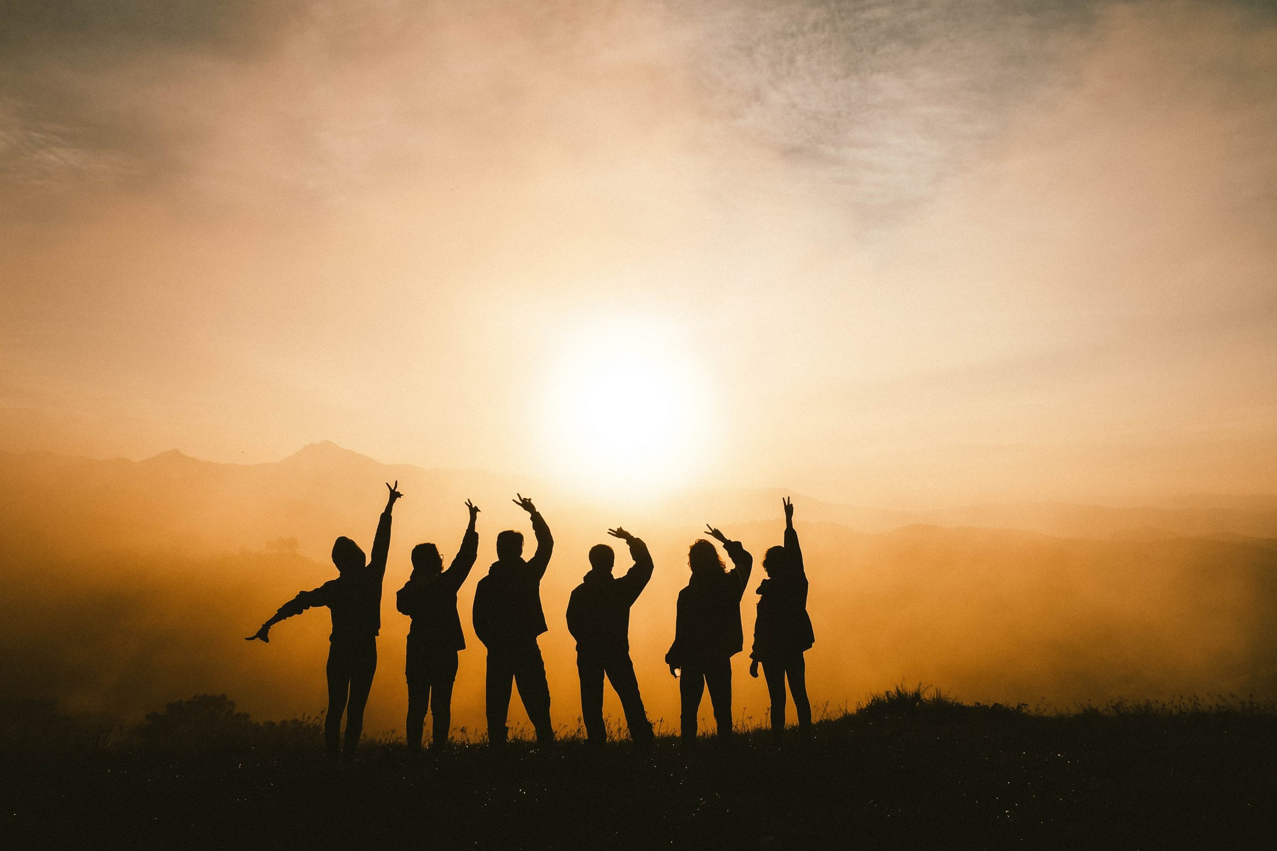 group of people standing in front of the sunrise and holding up the peace sign