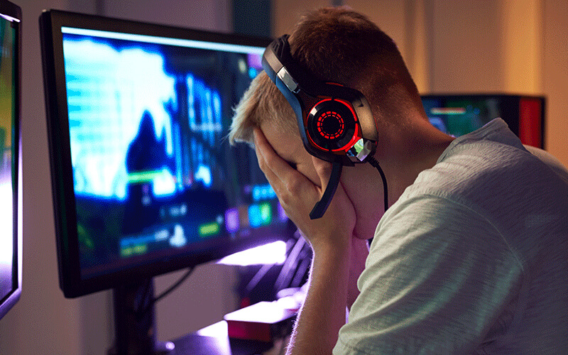 Boy with headphones on in front of computer screen with face in his hands