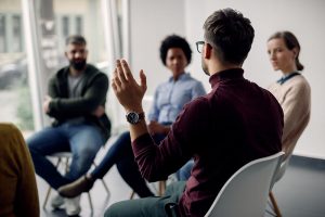 Man with his hand raised in a group therapy session