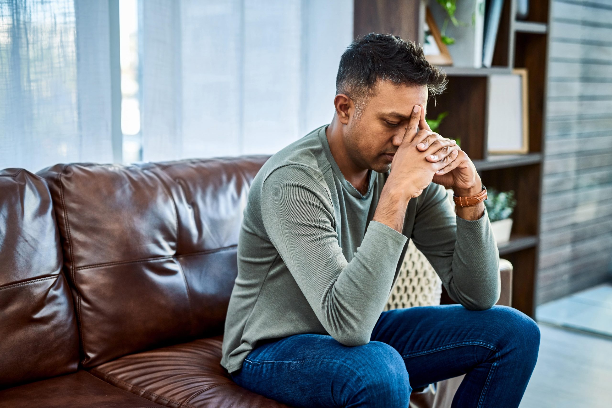 Man sitting on couch thinking with his hands on his head