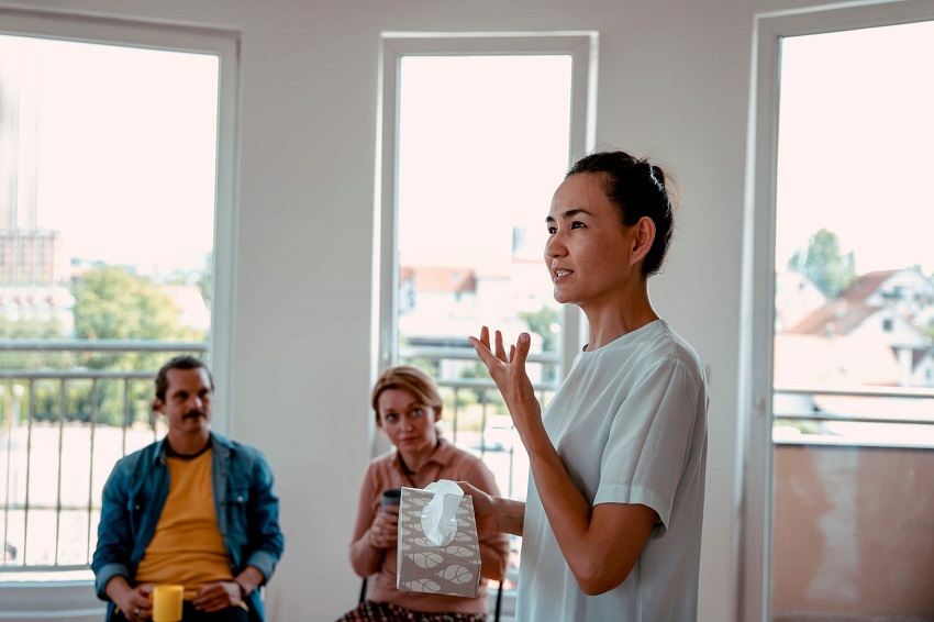 woman speaking to a group of people while holding tissues