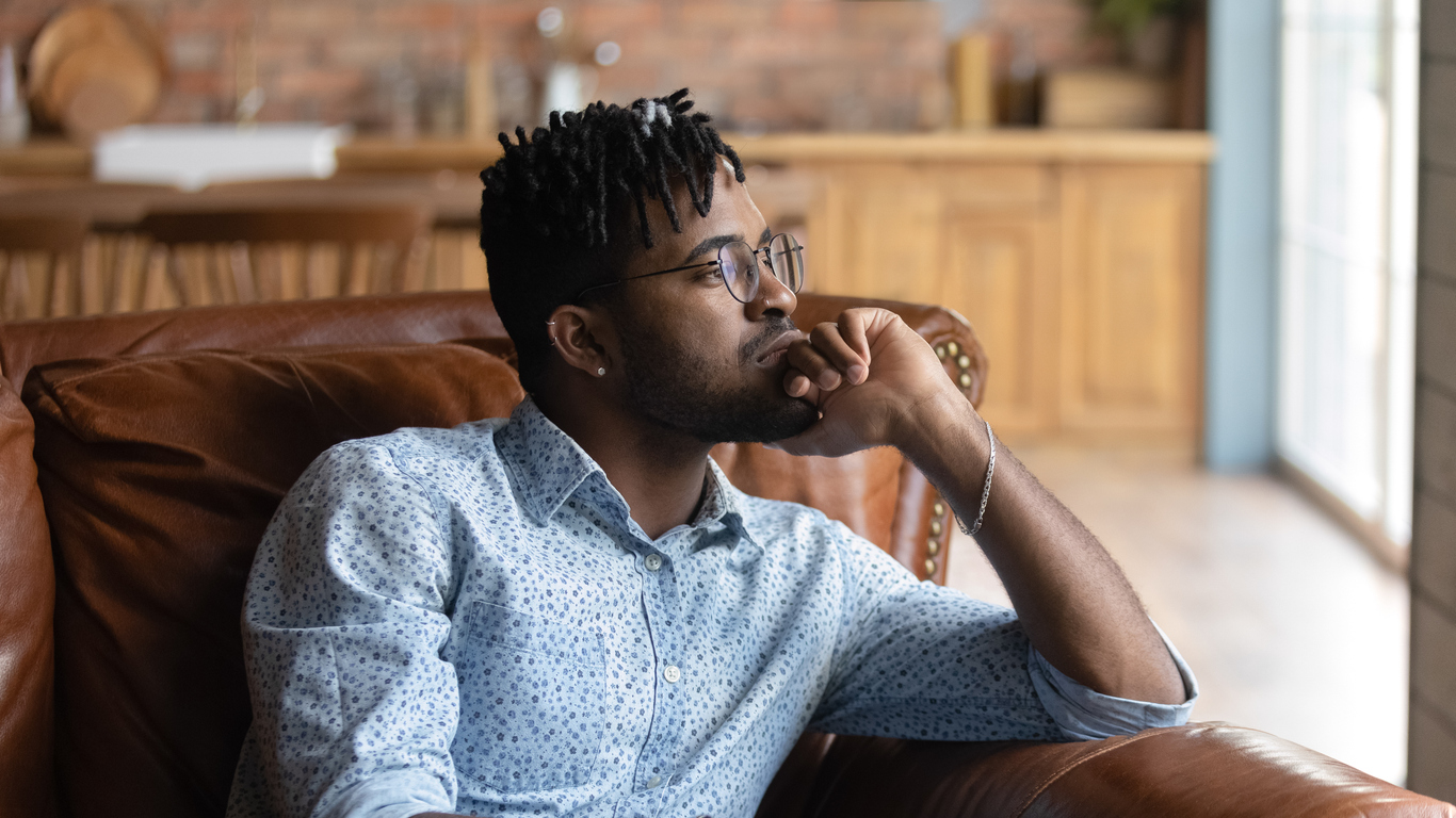 Young man thoughtfully looking out a window on a couch